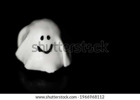 Halloween Concept - One little white ghost with a smile. Delicious cake  on Halloween against black background with copy space.