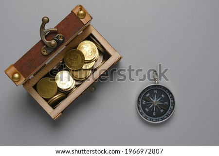 A picture of gold chest with coins and compass on gray table