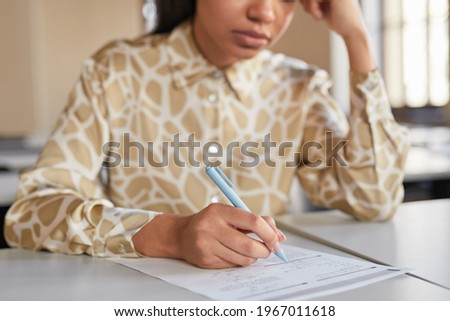 Cropped portrait of young African-American woman taking exam in school while sitting at desk in college and thinking, copy space