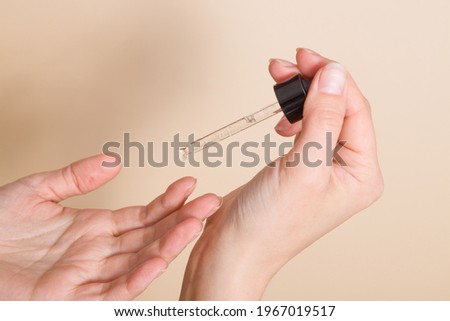A woman's hand holds a glass dropper and drips oil onto her finger. Medical or cosmetic oil application