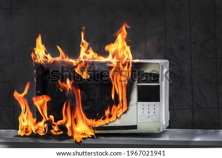Microwave oven white, in fire front view, electrical appliances caught fire as a result of improper operation Royalty-Free Stock Photo #1967021941