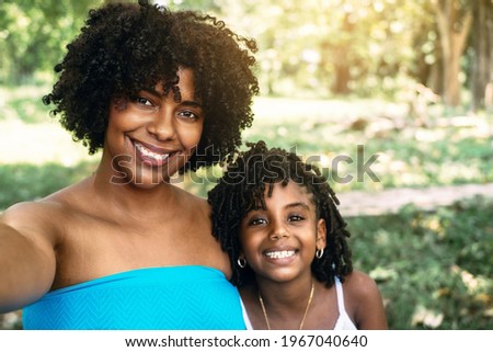 Portrait of a smiling and happy Latin American woman and her African American daughter taking a selfie. happiness and technology concept.