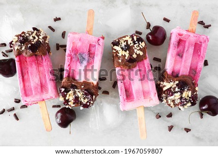Chocolate and almond dipped cherry popsicles. Top view in a row over a white marble background.