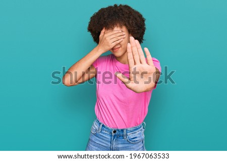 Young hispanic girl wearing casual clothes covering eyes with hands and doing stop gesture with sad and fear expression. embarrassed and negative concept. 