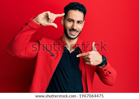 Young hispanic man wearing red leather jacket smiling making frame with hands and fingers with happy face. creativity and photography concept. 