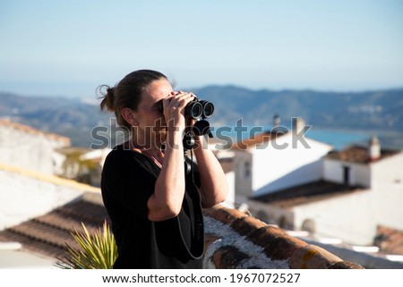 A woman is looking on the scenery with binoculars 