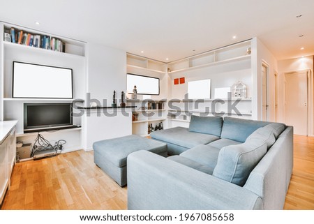 Comfortable couch located near bookcases with TV and decorations in light living room in modern apartment