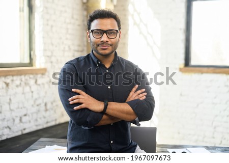 Ambitious hindu man in smart casual shirt stands with arms crossed in contemporary office space and looks at camera, portrait of purposeful indian businessman, ceo indoor. Diversity of office staff Royalty-Free Stock Photo #1967097673
