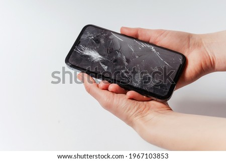 A smartphone with a broken screen in a woman's hand on a white background. Crash protective tempered glass for smartphone. Expensive smartphone with a broken screen