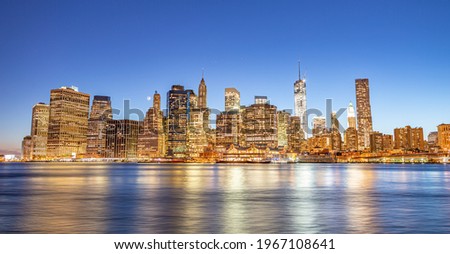 Downtown Manhattan at night from Brooklyn Bridge Park. New York City skyscrapers reflections in the river.