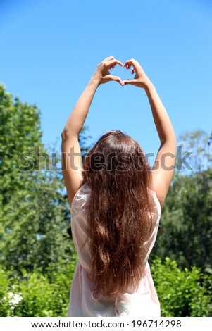 Young girl holding hands in heart shape framing on blue sky background