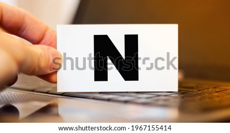 Businessman holds a business card with the letter N on the background of a laptop in the evening
