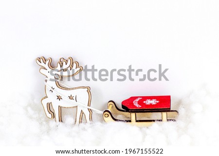 Toy wooden reindeer with red sleigh on white artificial snow background with copy space. Christmas and New Year holidays celebration concept
