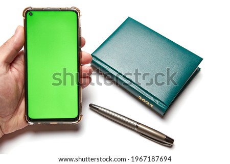 Male hand holds a phone with a green screen on a desktop background with a business notebook 2021 and a pen