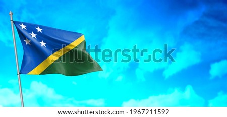 The solomon islands flag flapping in a strong wind against a blue sky with clouds.
