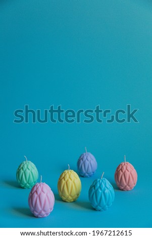Painted Easter eggs in the form of wax candles are arranged in a checkerboard pattern against a blue background. empty space for text