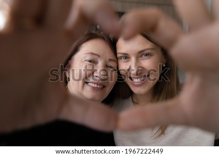 Portrait of happy elderly Caucasian mother and adult daughter make heart love hand gesture or sign together. Self-portrait picture of smiling adult kid child with mature mom show unity and bonding.