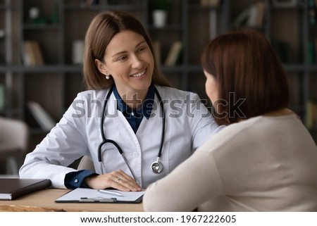 Smiling young Caucasian woman doctor support elderly patient at meeting in hospital. Happy female nurse or GP talk consult with mature client at clinic consultation. Healthcare, geriatrics concept. Royalty-Free Stock Photo #1967222605