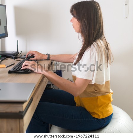 Portrait of a beautiful caucasian adult woman working with a computer from her home. Sitting on a pilates stability ball.