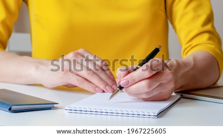 Closeup image of a woman writing down on a white blank notebook. Yellow background, selective focus. Can be used for business, marketing, education, financial concept
