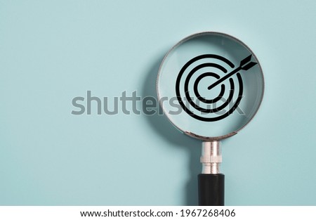 Target board inside of magnifier glass for focus business objective on blue background and copy space. Royalty-Free Stock Photo #1967268406
