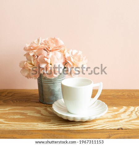 White coffee cup with carnation flower on wooden table. pink background