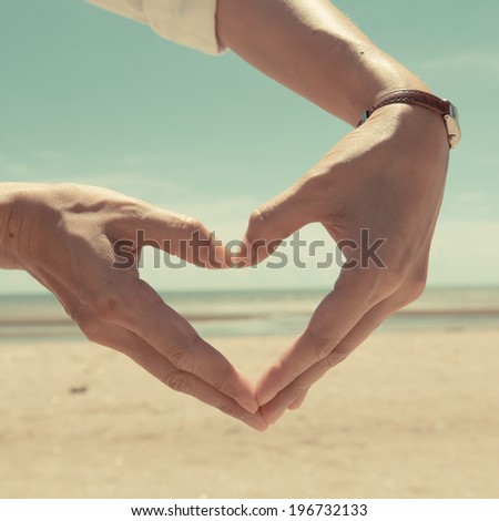 Woman making heart shape on the beach. Vintage style