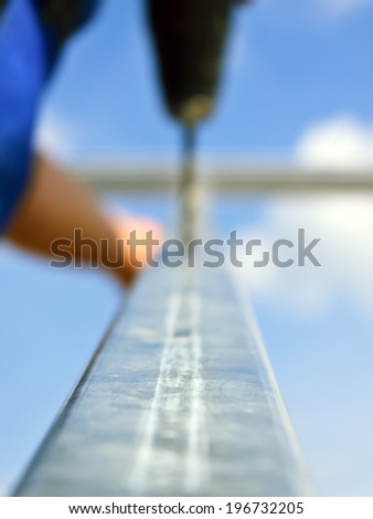 Out of focus photo of construction worker drilling hole with electric screwdriver on aluminium construction frame