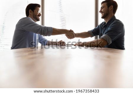 Smiling male employees or business partners shake hands close deal or make agreement after successful negotiations. Happy businessmen handshake get acquainted greet at meeting at workplace.