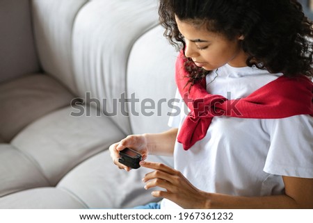 African American woman measures  pulse and oxygen saturation using a pulse oximeter sitting on the couch at home, healthcare concept Royalty-Free Stock Photo #1967361232