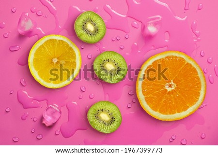 Fresh juicy slices of orange, kiwi fruit and lemon on bright red background covered with water drops. Creative food background, top view