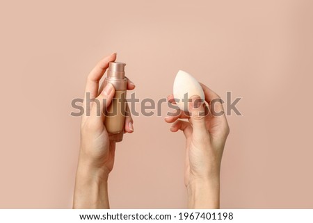 Applying foundation on makeup sponge. Woman's hands with neutral manicure holding bottle of concealer or toner foundation, cream and beauty blender, make up artist background Royalty-Free Stock Photo #1967401198