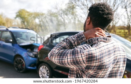 Young man rubbing neck in pain from whiplash injury standing by damaged car after traffic accident Royalty-Free Stock Photo #1967420284