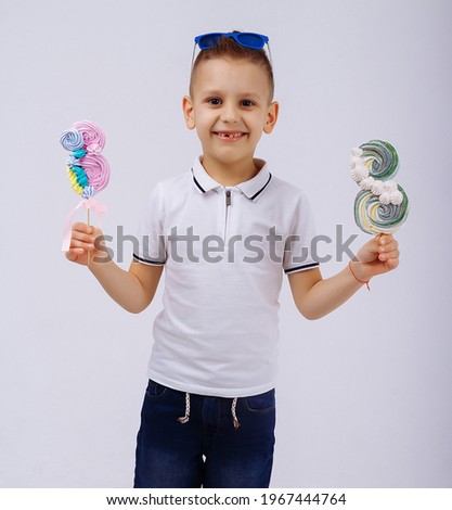 a boy in sunglasses, denim shorts and a white T-shirt, on a white background holds a candy in the form of a figure eight. Women's day, congratulations. men congratulate. March 8
