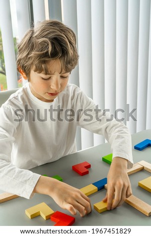 Boy playing with a wooden cube on the gray background. Multi-colored cubes on the table. Geometric shapes on a wooden background. Puzzle concept. High quality photo