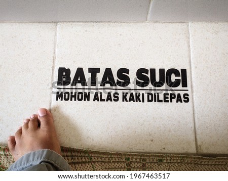 It is a kind of sign which commonly to be found on the floor in front of mosque in  Indonesia. Batas Suci, mohon alas kaki dilepas ( sacred limit, please take off shoes )