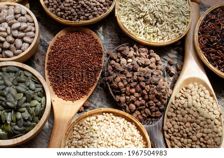 Dry organic brown chick pea with rice, red quinoa, lentils, pinto, pumpkin seeds, and buckwheat in wooden spoon on grunge background in dark tone under morning sun light