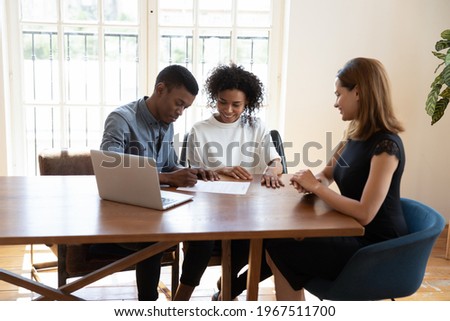 Smiling millennial african american family couple signing contract agreement with female real estate agent at office meeting, discussing deal terms of conditions, purchasing renting leasing apartment. Royalty-Free Stock Photo #1967511700