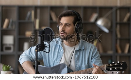 Close up man in headphones playing guitar, singing in microphone, popular musician artist recording new song or podcast in home studio, composing, using musical instrument, hobby and music concept