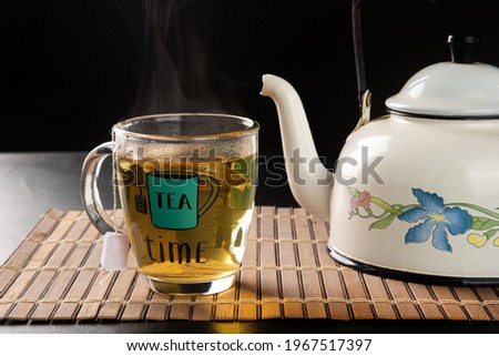 kettle and cup of tea, both coming out of smoke on a wooden mat, black background, selective focus.