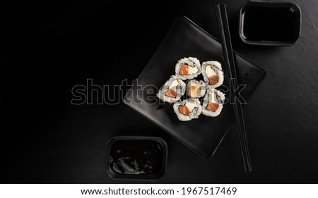 Sushi, beautiful sushi arrangement with hashi and shoyo sauce and tare made in black dishes on a dark surface, black background, top view. Royalty-Free Stock Photo #1967517469