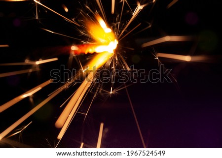 Close-up dreamy photo of a brightly burning sparkler with light trails flying all directions on the black background with bokeh