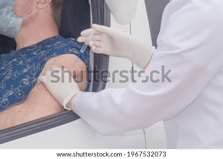 Mobile vaccination center. A nurse vaccinates a man who is sitting in a car outdoors.