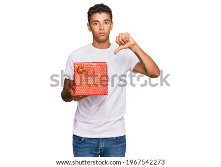 Young handsome african american man holding gift with angry face, negative sign showing dislike with thumbs down, rejection concept 