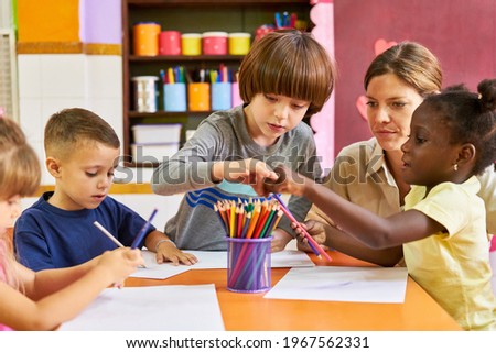 Educator and group of children in international kindergarten painting with crayons