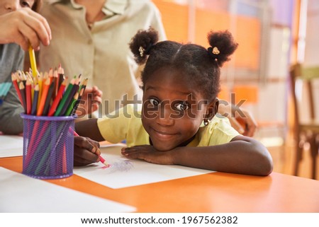 African girl paints a picture with crayons on paper in international kindergarten