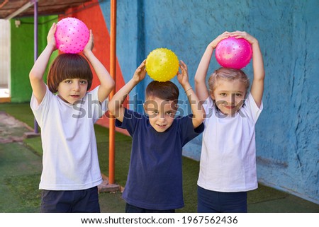 Three children as friends playing ball on the sports field in daycare or elementary school