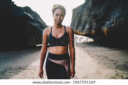 Half length portrait of attractive African American fit girl with casual figure support body positive movement, dark skinned female trainer in sportive clothes posing at seashore beach during morning