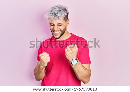 Young hispanic man with modern dyed hair wearing casual pink t shirt celebrating surprised and amazed for success with arms raised and eyes closed. winner concept. 