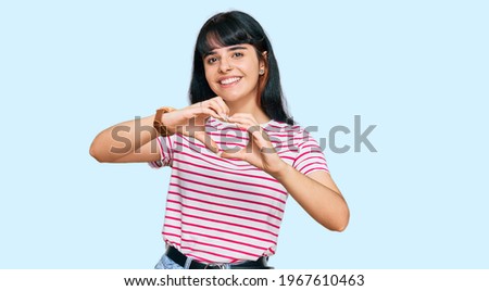 Young hispanic girl wearing casual clothes smiling in love doing heart symbol shape with hands. romantic concept. 